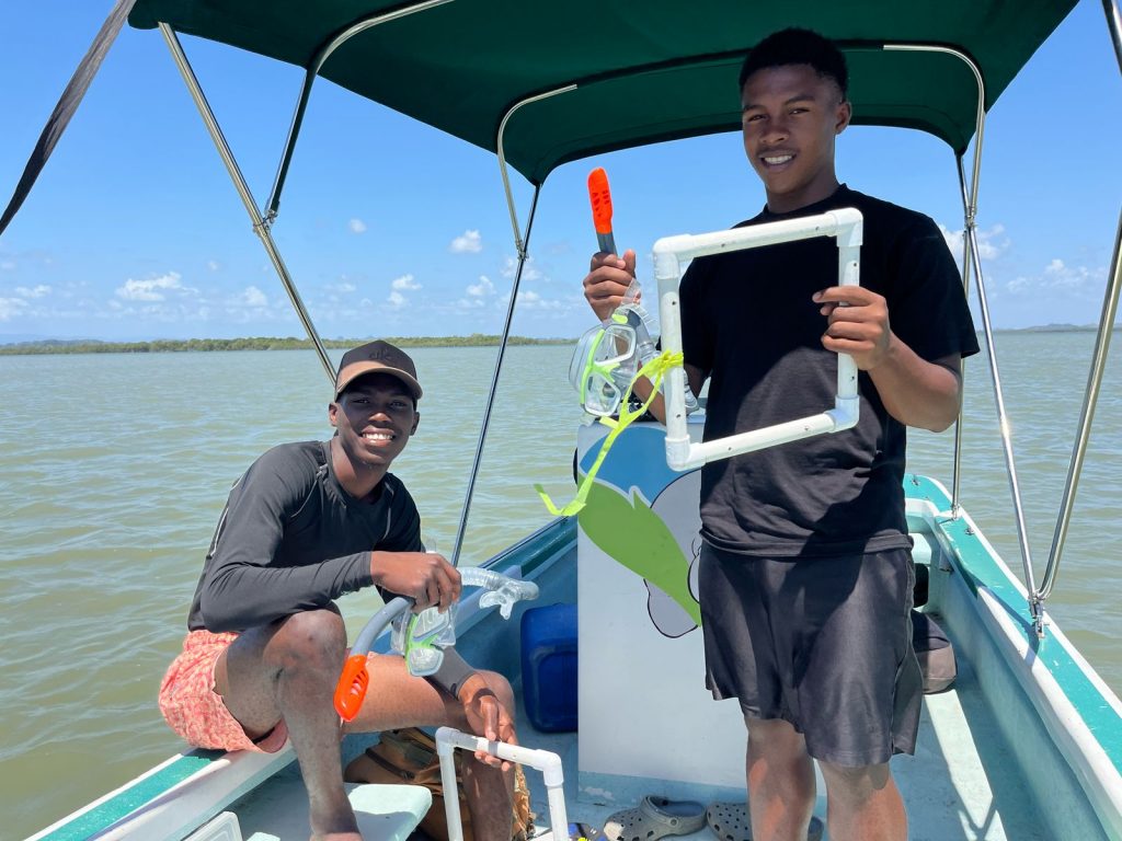 Two youth community members participating in seagrass monitoring from a small boat.